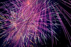 Purple fireworks in a dark sky. Purple festive firecracker. Bright purple, pink and orange firework display in the night sky.Purple and blue fireworks in the night sky. photo