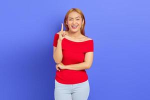 Portrait of surprised young Asian woman in red dress and blonde hair, pointing having idea isolated on purple background photo
