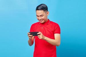 Portrait of cheerful young asian man playing a game on mobile phone isolated on blue background photo