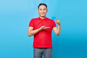 Portrait of smiling young asian man showing credit card, offer ad product isolated on blue background photo