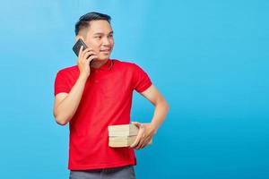 Portrait of attractive Asian man talking on smartphone and looking happy while holding book isolated on blue background photo