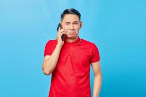 Portrait of confused asian man talking on smartphone and looking at camera isolated on blue background photo