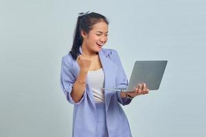 Portrait of smiling young Asian woman looking at laptop and celebrating success of getting new project isolated on white background photo