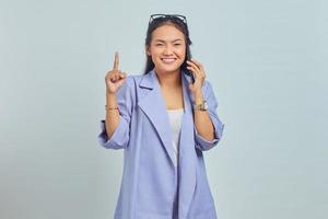 Portrait of happy young Asian woman talking on mobile phone and having an idea while pointing finger up isolated on white background photo