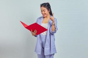 Portrait of cheerful young Asian business woman holding document folder and gets brilliant idea in mind isolted on purple background photo