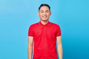 Portrait of handsome Asian man in red shirt and smiling happy looking straight ahead in good mood having auspicious day isolated on blue background photo