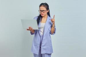 Portrait of surprised young Asian woman standing using laptop and pointing finger at copy space with open mouth isolated on white background photo