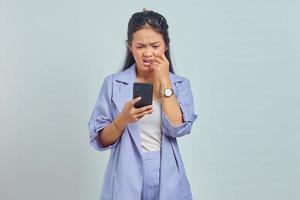 Portrait of young Asian woman using cell phone looking stressed and nervous with hand in mouth biting nail on white background photo