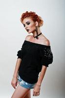 Studio portrait of red haired girl on black blouse and jeans shorts with bright dark make up photo