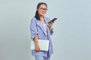 Portrait of cheerful young Asian woman holding laptop and using mobile phone isolated on white background photo