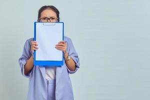 Portrait of scared young Asian business woman covering face with folder isolated on purple background photo