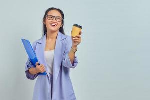 Portrait of cheerful young Asian business woman holding clipboard and drinking takeaway coffee isolated on purple background photo