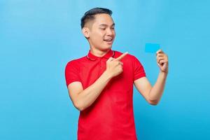 Portrait of cheerful young asian man pointing finger on credit card isolated on blue background photo