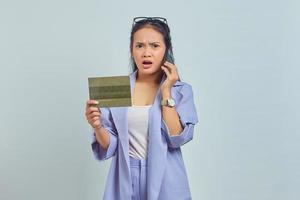Portrait of shocked young Asian woman talking on mobile and showing vehicle book isolated on white background photo