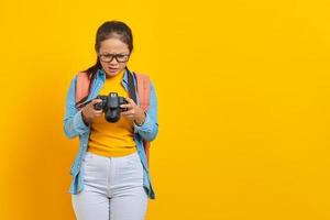 Portrait of surprised young Asian woman looking at photo on camera isolated on yellow background. Passenger traveling on weekends. Air flight journey concept