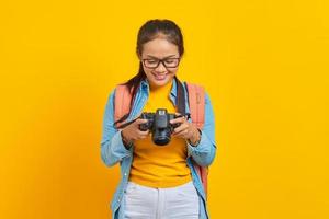Portrait of smiling young Asian woman looking at photo on camera isolated on yellow background. Passenger traveling on weekends. Air flight journey concept