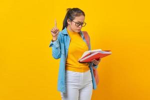 Young woman student in denim clothes with backpack, Holding book pointing index finger up with great new idea isolated on yellow background. Education in high school university college concept photo