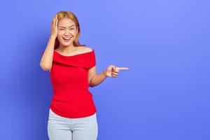 Portrait of a beautiful young Asian woman wearing red dress standing, presenting copy space isolated over purple bacground photo