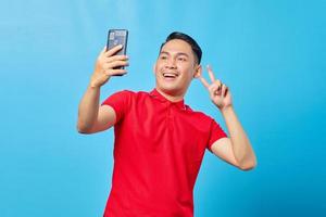 retrato de un joven asiático emocionado y alegre que usa un teléfono móvil para tomar selfie sobre fondo azul foto