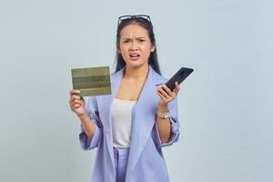 retrato de una joven asiática pensativa que muestra el libro del vehículo y sostiene un teléfono inteligente aislado de fondo blanco foto