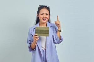 Portrait of cheerful young Asian woman pointing finger at empty space and holding vehicle book isolated on white background photo