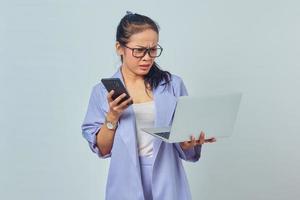 retrato de una joven asiática sorprendida sosteniendo un smartphone y mirando el correo electrónico entrante en una laptop aislada de fondo blanco foto