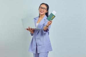 retrato de una joven asiática parada usando una laptop y sosteniendo un pasaporte con una expresión alegre aislada de fondo blanco foto
