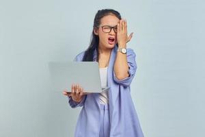 retrato de una joven asiática sorprendida parada usando una laptop y cubriendo media cara con palmas aisladas sobre fondo blanco