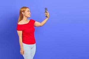 Portrait of attractive young Asian woman standing taking selfie with smartphone and smiling isolated on purple background photo