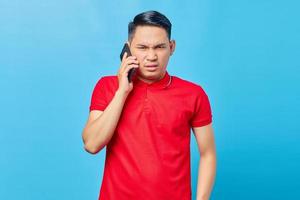 retrato de un hombre asiático enojado hablando por teléfono inteligente y mirando la cámara aislada en el fondo azul foto