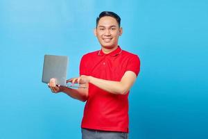 Smiling young handsome man holding a laptop and looking at camera isolated on blue background photo