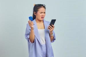 Portrait of pensive young Asian woman holding banking token and holding smartphone over white background. concept money transfer via internet photo