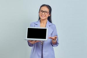 Portrait of cheerful young Asian woman showing laptop and looking at camera isolated on white background photo