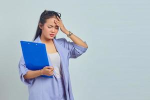 retrato de una joven empresaria asiática deprimida sosteniendo una carpeta de documentos, sintiéndose mareada y dolor de cabeza severo aislada en un fondo morado foto