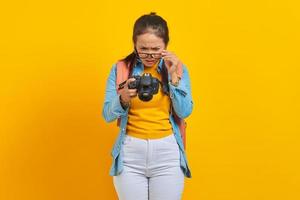 Portrait of surprised young Asian woman looking at photo on camera isolated on yellow background. Passenger traveling on weekends. Air flight journey concept