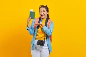 Portrait of cheerful young Asian traveler showing passport boarding pass ticket with palms isolated on yellow background. Passengers traveling on weekends. Air flight travel concept photo
