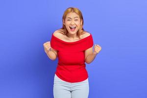 Portrait of excited young Asian woman celebrating victory isolated on purple background photo
