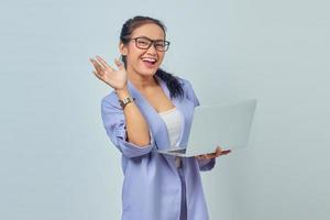 Portrait of cheerful young Asian woman using laptop and gesturing wave hand isolated on white background photo