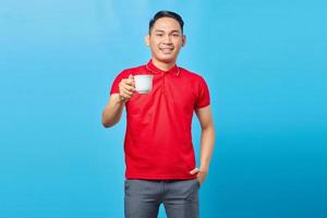 retrato de un apuesto joven asiático sonriente sosteniendo una taza de café aislado de fondo azul foto