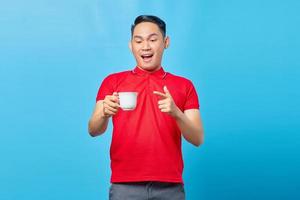 Shocked handsome Asian young man holding cup of coffee drink isolated on blue background photo