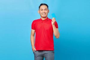 Portrait of excited Asian young man showing blank credit card and looking at camera isolated on blue background photo