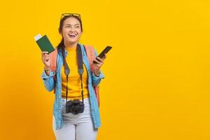 Portrait of cheerful young Asian traveler holding passport boarding pass ticket and smartphone isolated on yellow background. Passengers traveling on weekends. Air flight travel concept