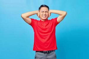 Portrait of frustrated Asian handsome young man covering ears with angry expression isolated on blue background photo