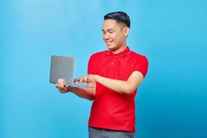 retrato de un joven apuesto sonriente sosteniendo y usando una laptop con fondo azul foto