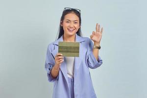 Portrait of smiling young Asian woman holding vehicle book and showing thumbs up gesture, Approving expression looking at camera showing success isolated on white background photo