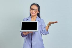 Portrait of smiling young Asian woman showing blank laptop screen and pointing to copy space for product presentation isolated on white background photo