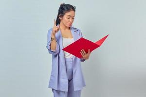 Portrait of cheerful young Asian business woman holding document folder and gets brilliant idea in mind isolted on purple background photo