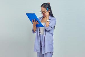 Portrait of confused young Asian business woman looking at job listing on clipboard isolated on purple background photo