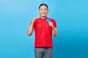 Portrait of excited young asian man holding a blank card and raising a fist in victory gesture isolated on blue background photo