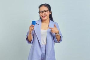 retrato de una alegre joven asiática señalando con el dedo a la ficha bancaria aislada de fondo blanco. concepto de transferencia de dinero a través de internet foto